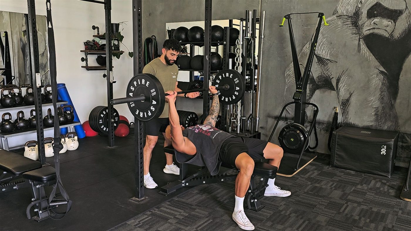 Ayden spotting a client on the bench press at Aspire